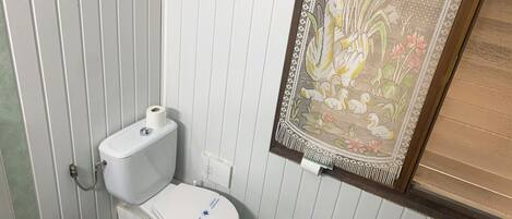 Un baño con inodoro, un bote de basura y una cortina decorativa.