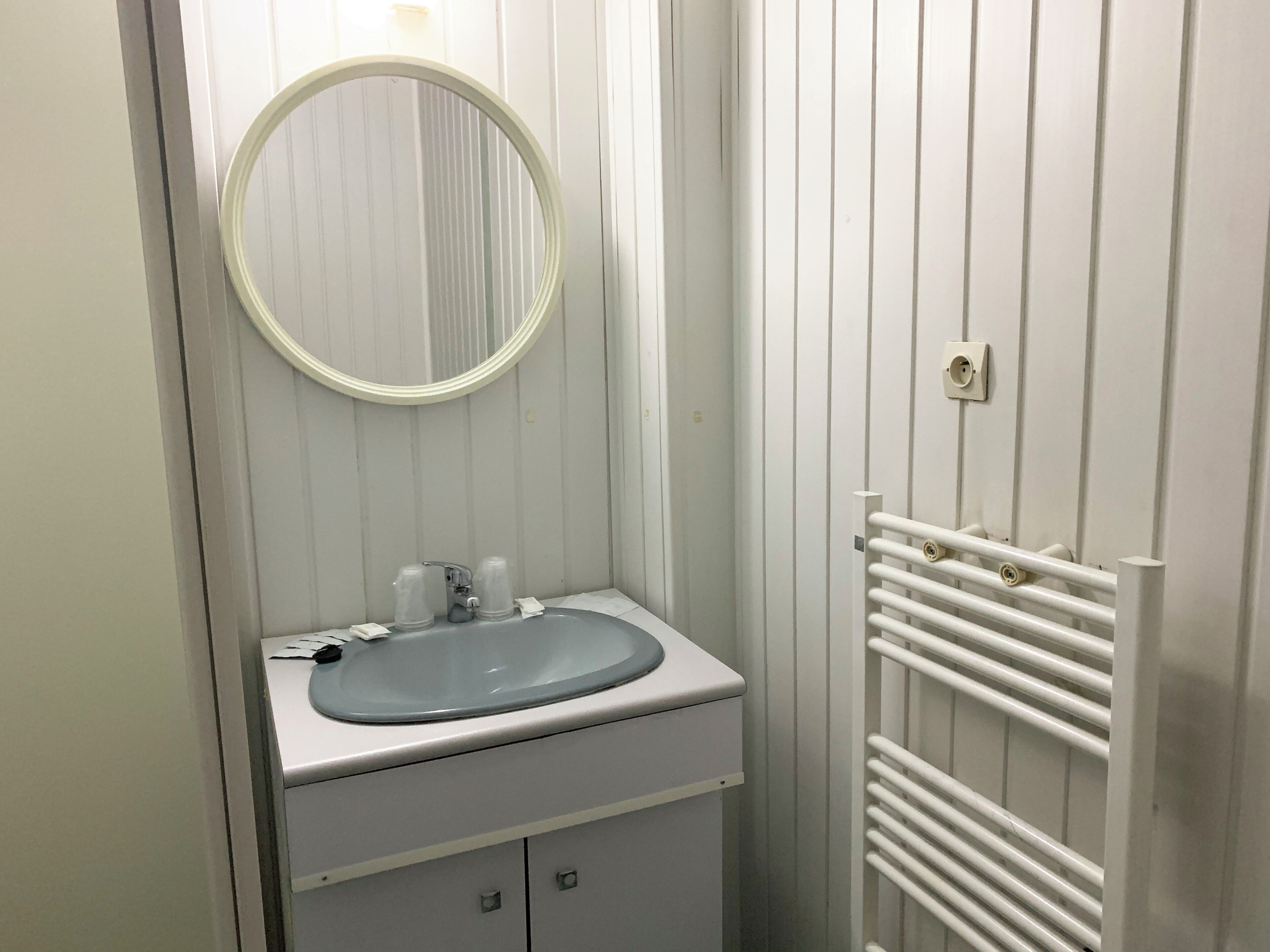 A bathroom with a white sink, a round mirror, and a towel rack.