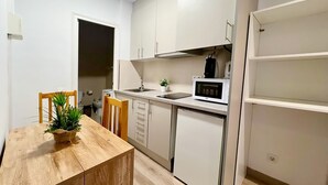 Une cuisine compacte avec des meubles blancs, un four à micro-ondes, un évier et un petit plan de travail. On y trouve une table à manger en bois avec des chaises et une plante en pot.
