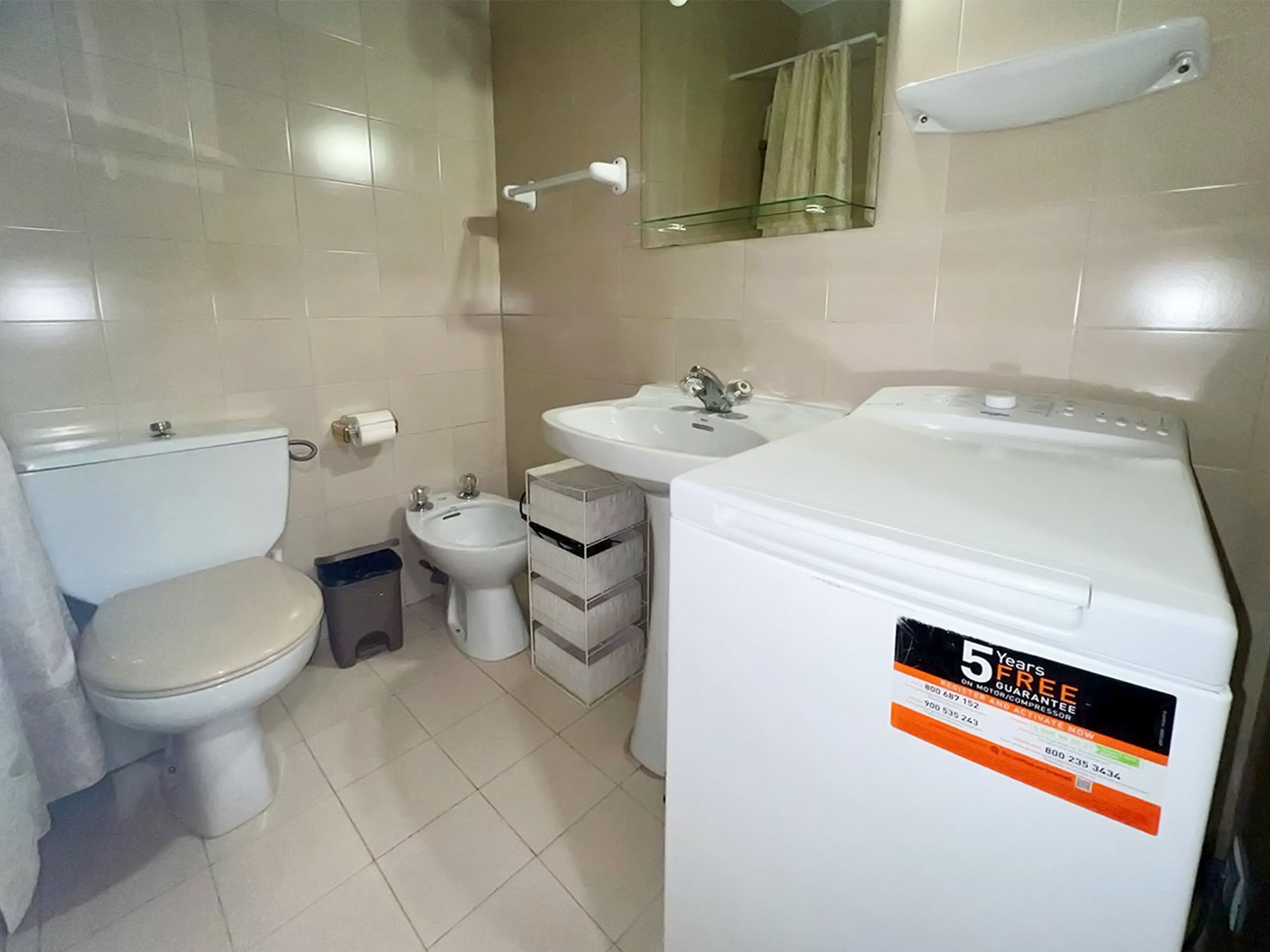 A compact bathroom with a toilet, bidet, sink, and a washing machine.
