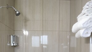 A modern shower with a handheld showerhead, a wall-mounted faucet, and a stack of white towels on the right. -  VOW MOTEL LISTOWEL ON (North Perth)