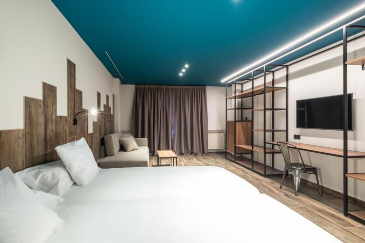 Ein modernes Hotelzimmer mit einem großen Bett, einem Schreibtisch mit Stuhl, einem Fernseher und integrierten Regalen.