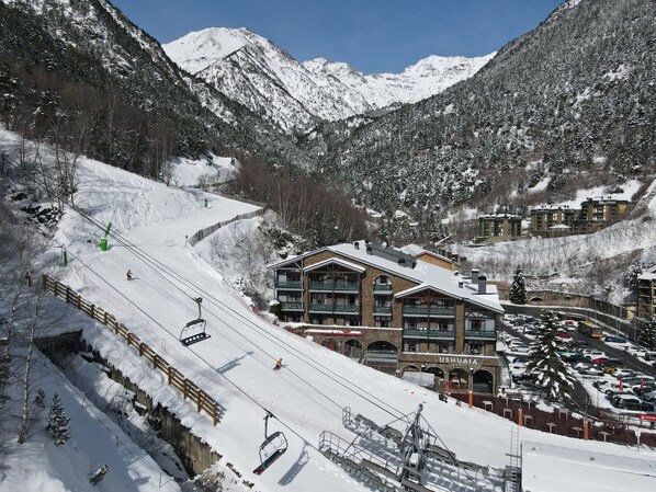 Une station de ski avec un bâtiment portant l’inscription « USHUAIA », comprenant un télésiège, des pistes enneigées et un paysage montagneux en arrière-plan.