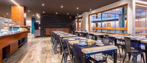 A spacious dining area with long tables and chairs, a buffet counter, and a view of the building's interior.