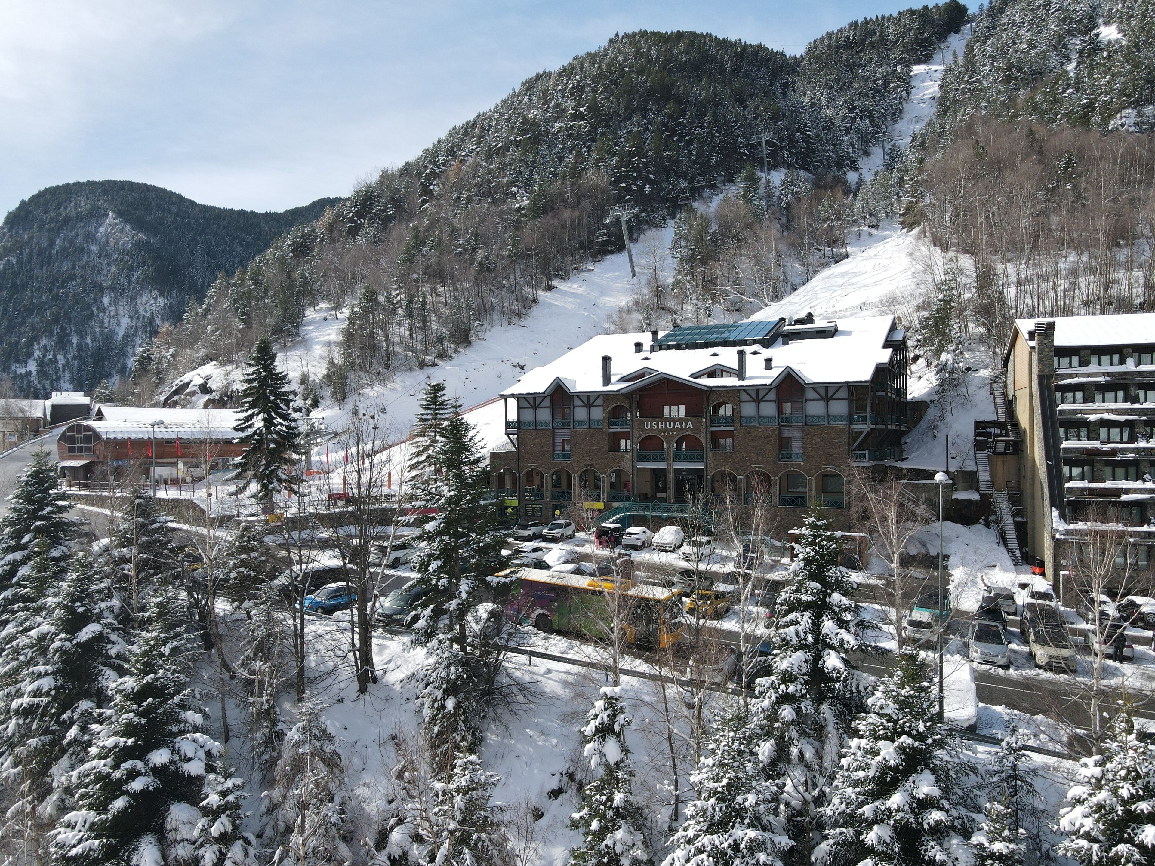 Une station de montagne enneigée, avec un bâtiment imposant portant l’inscription « USHUAITA » et un télésiège en arrière-plan.