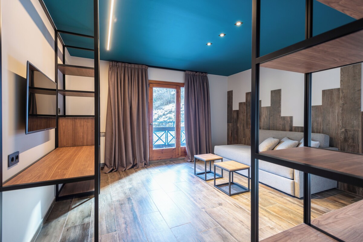 Une chambre moderne avec un plancher en bois, un canapé, un téléviseur fixé au mur et une fenêtre avec des rideaux.