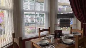 Un área de comedor con una mesa dispuesta para dos personas, una ventana con persianas y vista a la calle.