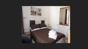 Un dormitorio con una cama grande, una mesita de noche, una lámpara, un cuadro en la pared y un espejo en la puerta.