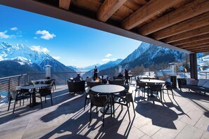 A terrace with tables and chairs, overlooking a mountainous landscape.
