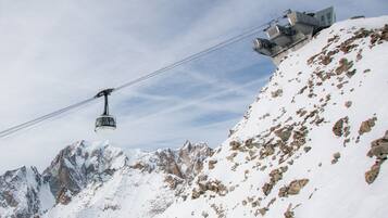 Eine Seilbahn in einer gebirgigen Landschaft mit felsigem Gelände und schneebedeckten Gipfeln.