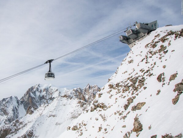 A cable car system in a mountainous area with rocky terrain and snow-covered peaks.