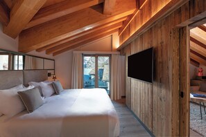 Un dormitorio con una cama grande, vigas de madera en el techo, un televisor de pantalla plana y vistas al exterior.