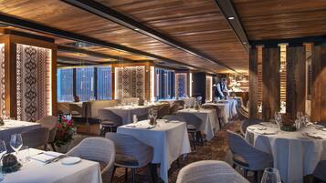 A restaurant with wooden ceiling beams, white tablecloths, and wicker chairs.