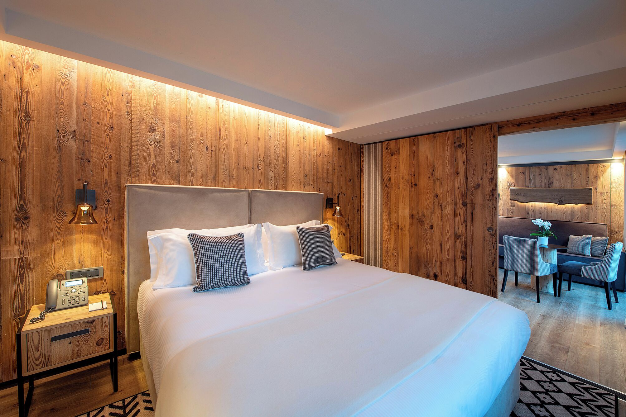 Une chambre d’hôtel avec un grand lit, des murs lambrissés, un bureau avec un téléphone et un coin salon comprenant des fauteuils et une table.