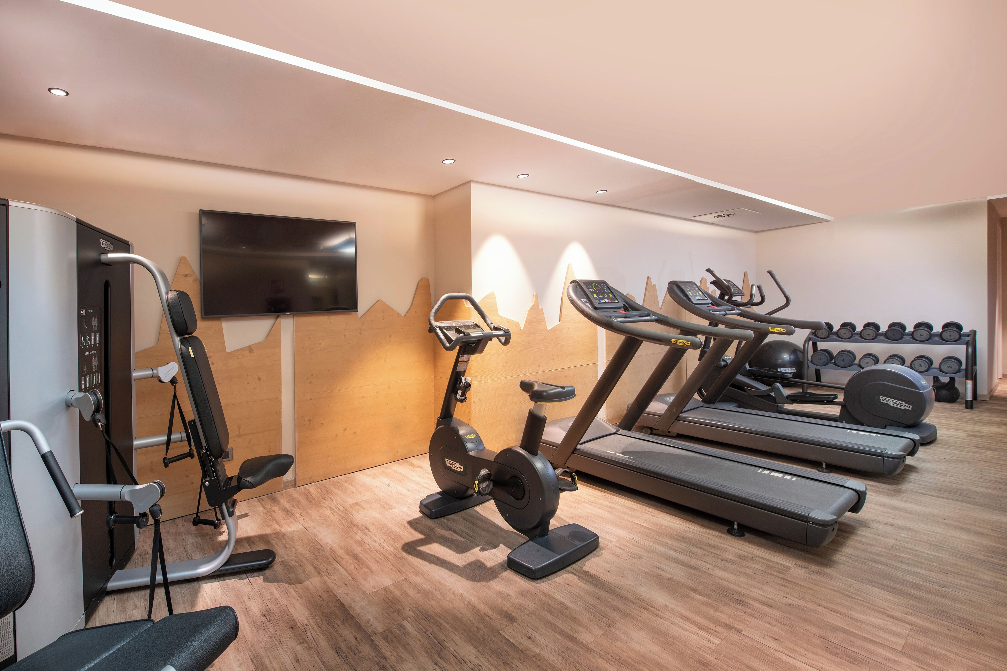 Uma academia com equipamentos de ginástica, uma televisão e uma TV fixada na parede.