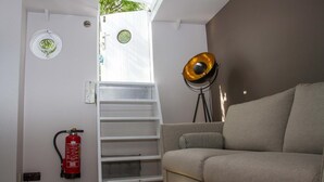 Un espacio habitable compacto con sofá, una escalera a una ventana, extintor y lámpara de pie.