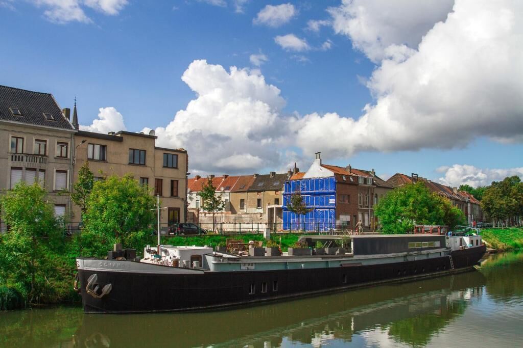A narrowboat docked by a canal with buildings in the background.