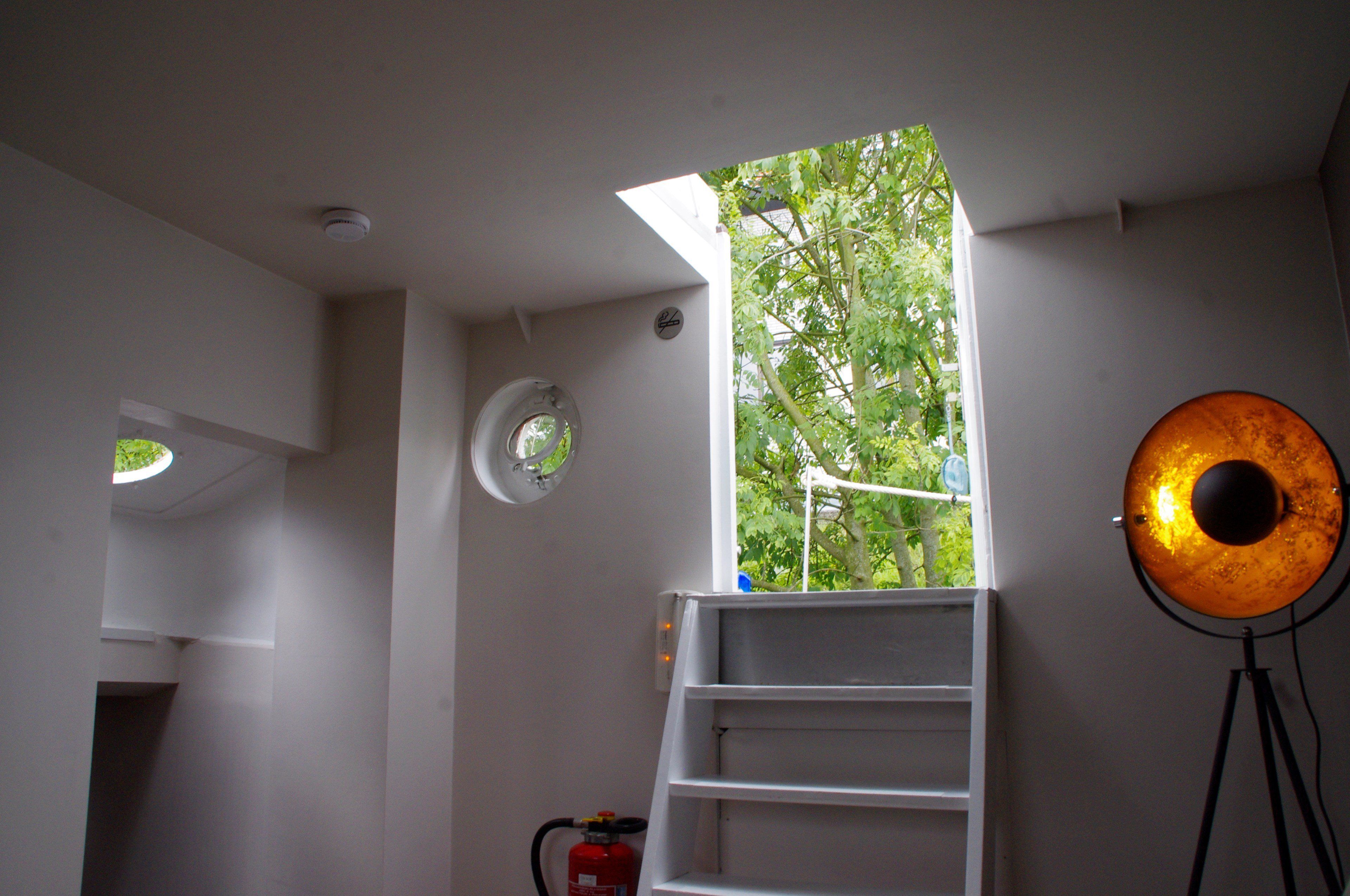 A room with a skylight, a ladder, a fire extinguisher, and a wall-mounted light fixture.