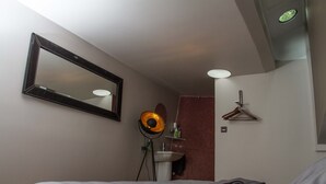 Un dormitorio con cama, espejo, lámpara de pie, lavamanos y toalla en el suelo.