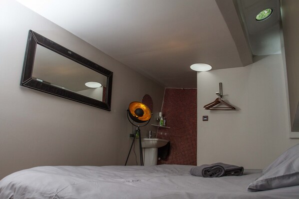A bedroom with a bed, a mirror, a floor lamp, a sink, and a towel on the floor. - BnB Boat (Ghent)