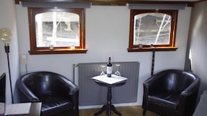 Una habitación con dos sillones de cuero, una mesita con una botella y dos ventanas con marcos de madera.