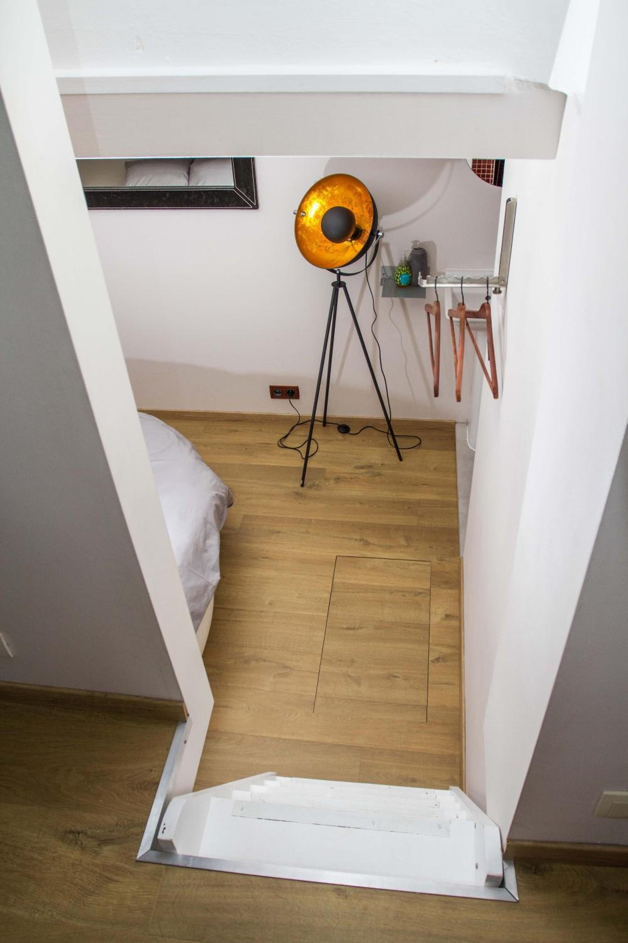 A compact room with a bed, a standing lamp, and a small shelf with items.