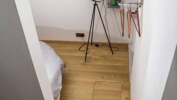 A compact room with a bed, a standing lamp, and a small shelf with items.