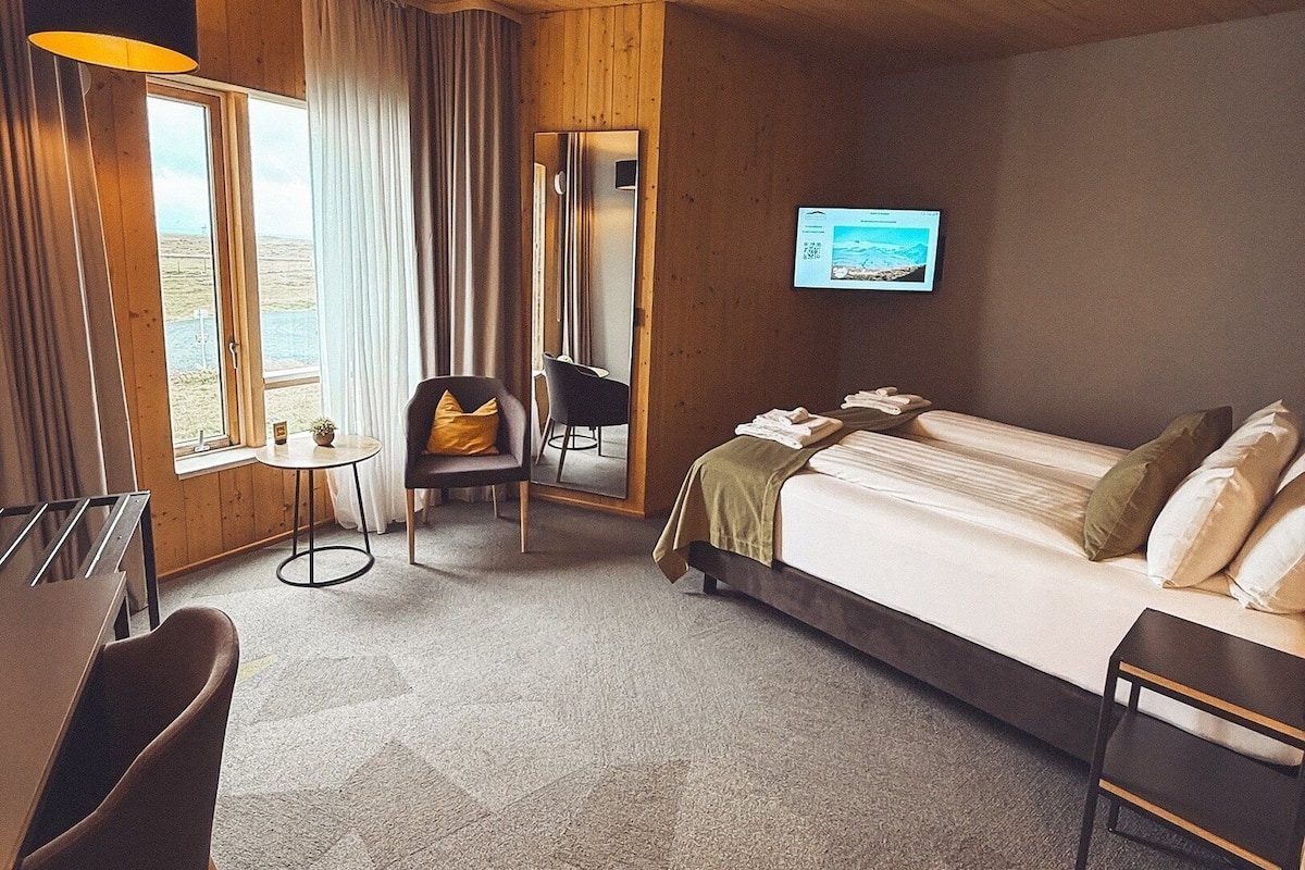 A hotel room with a bed, a desk, a chair, a TV, and a window with curtains.