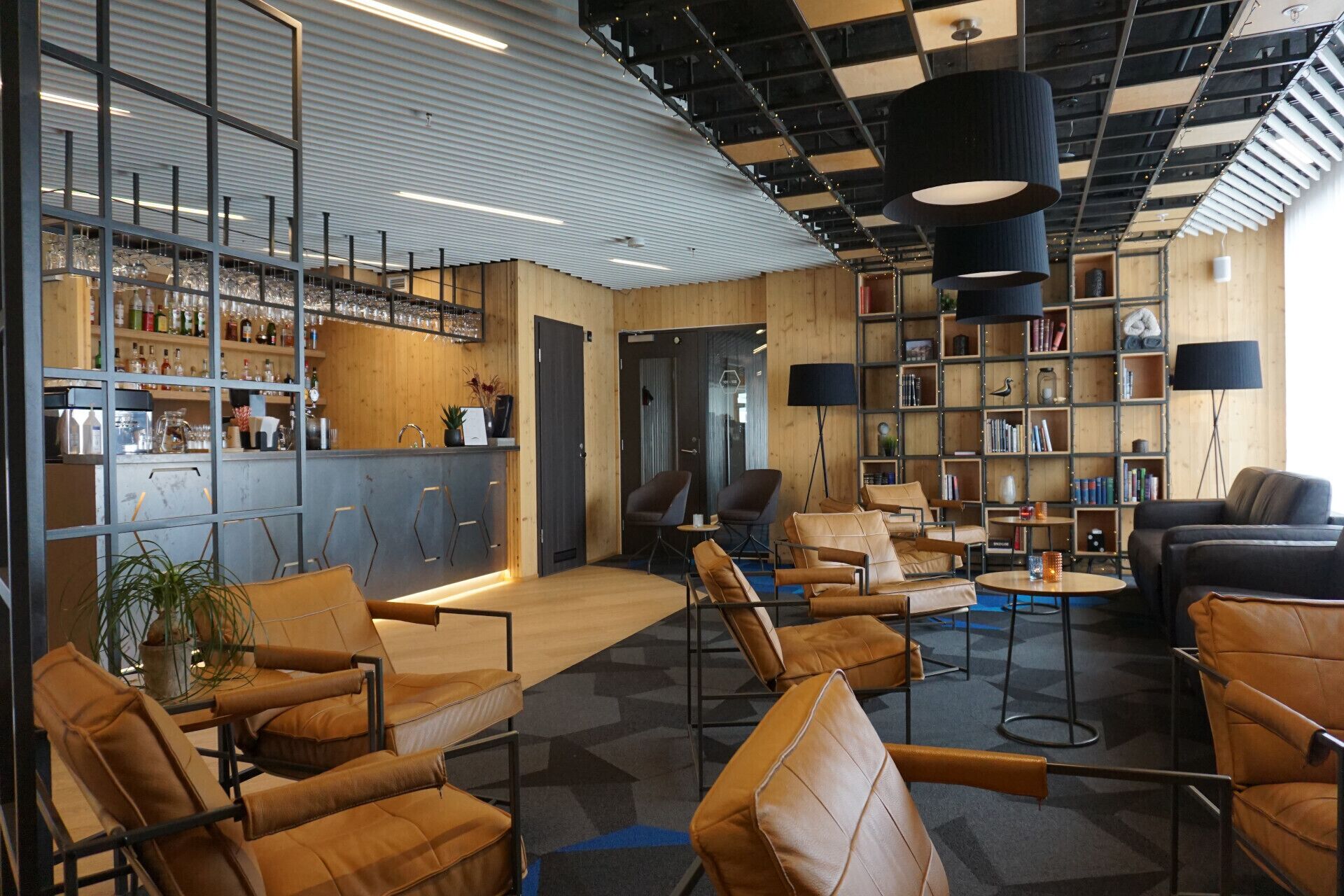 A modern lounge area with leather sofas, a bar with shelves of bottles, and a bookshelf.