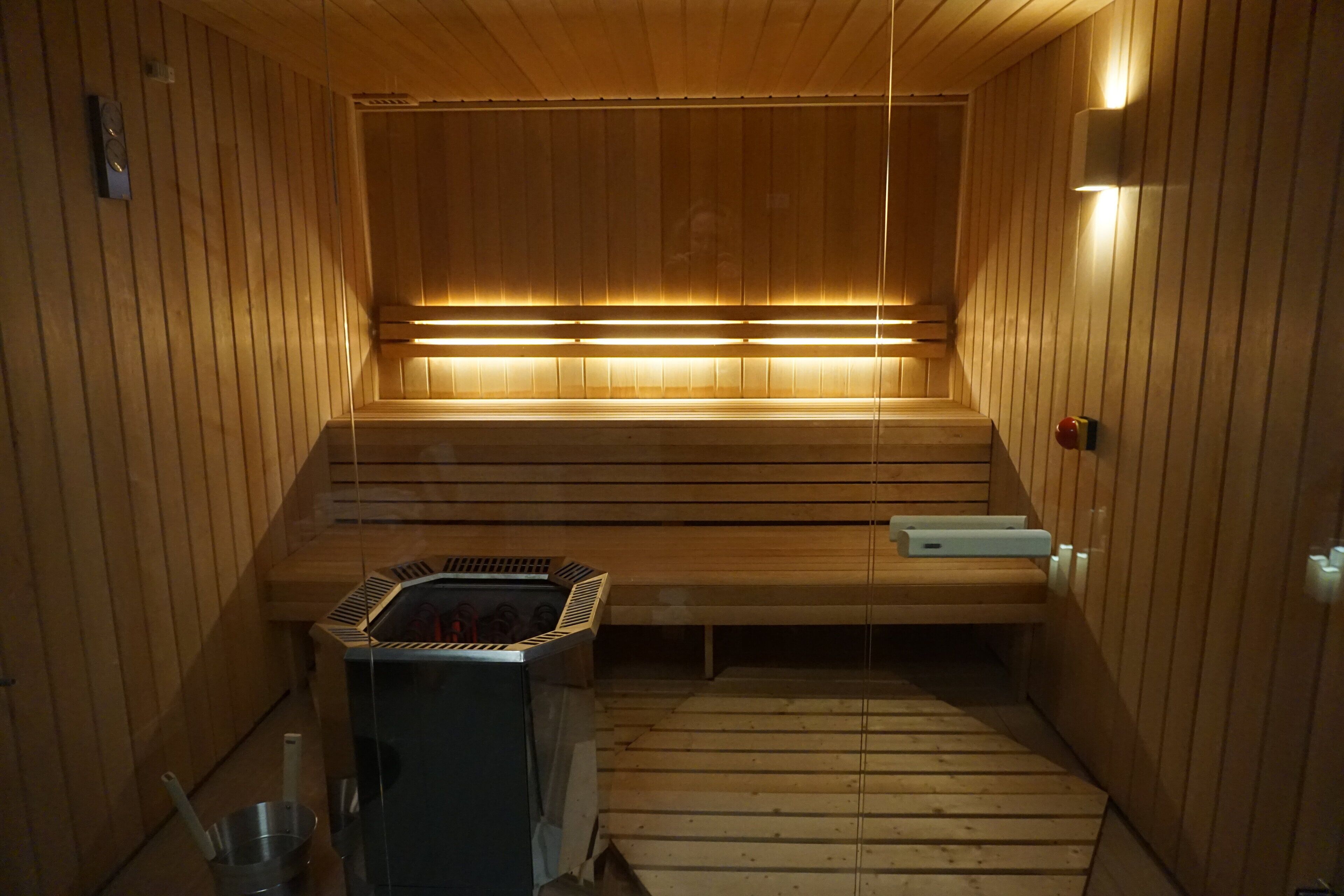 A sauna with wooden walls and benches, a heater, and a small table with a bucket and brush.