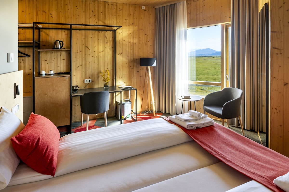 A hotel room with a bed, a desk, a chair, a small table, and a window with a view of the outdoors.