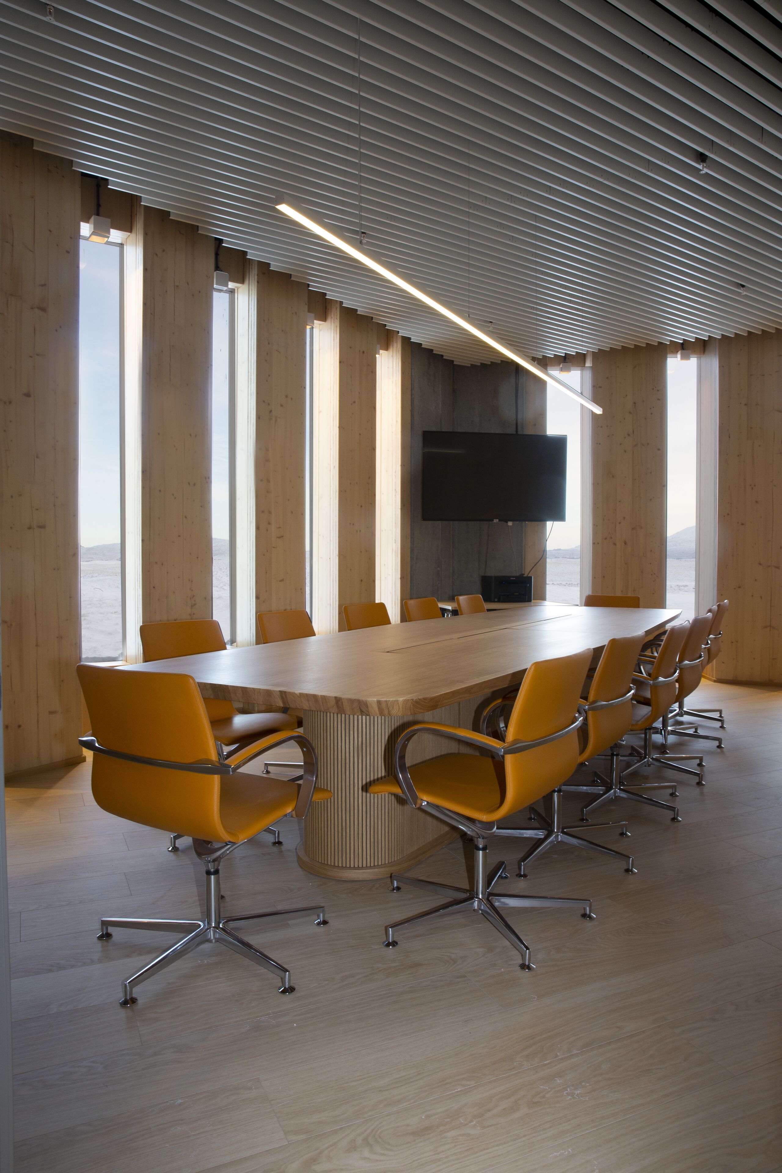 A conference room with a long table, multiple chairs, a flat-screen TV, and large windows.