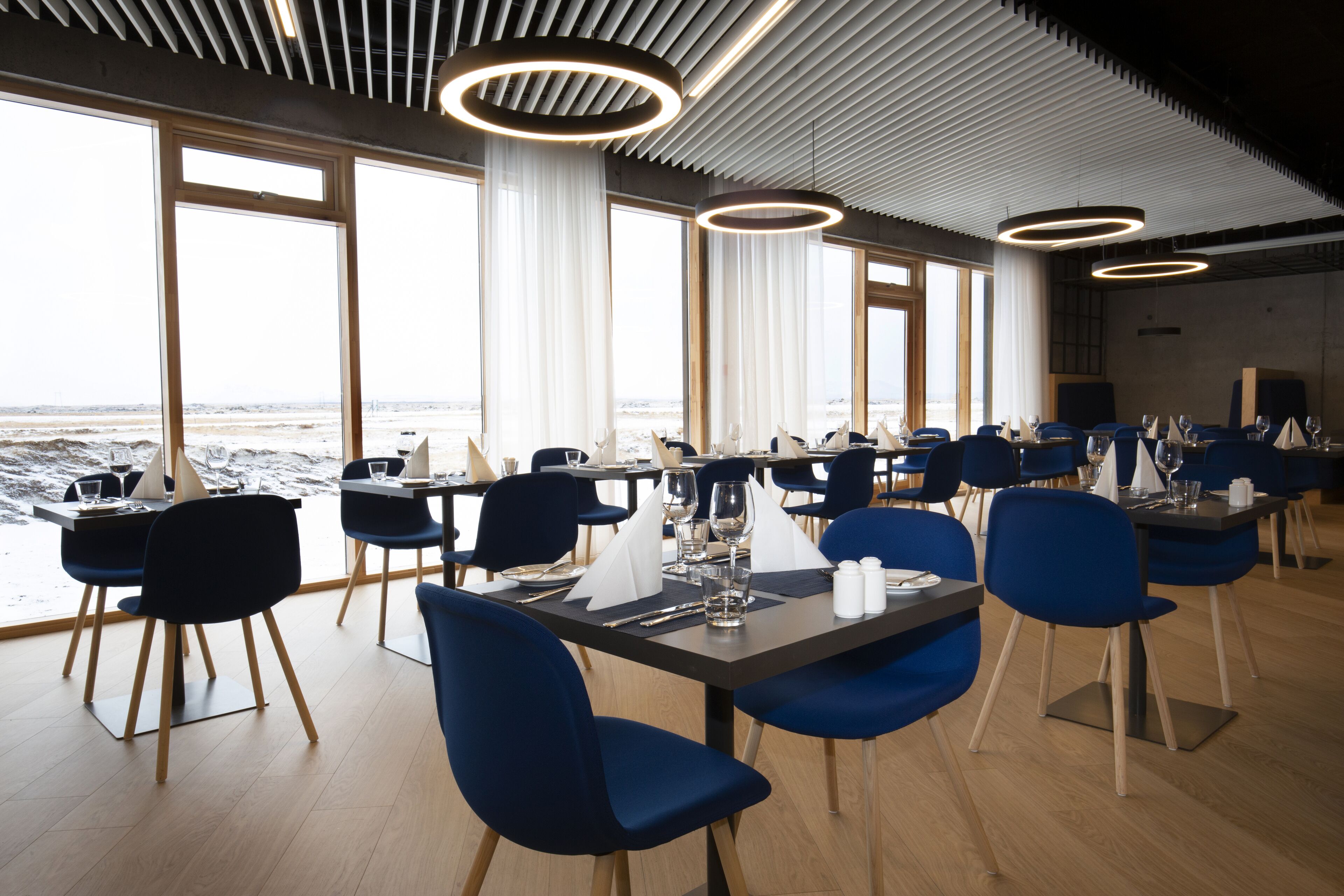 A modern dining area with tables and chairs, large windows, and a view of the beach.