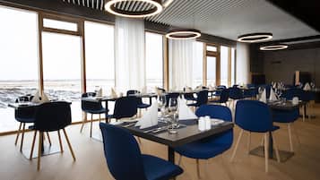 A modern dining area with tables and chairs, large windows, and a view of the beach.