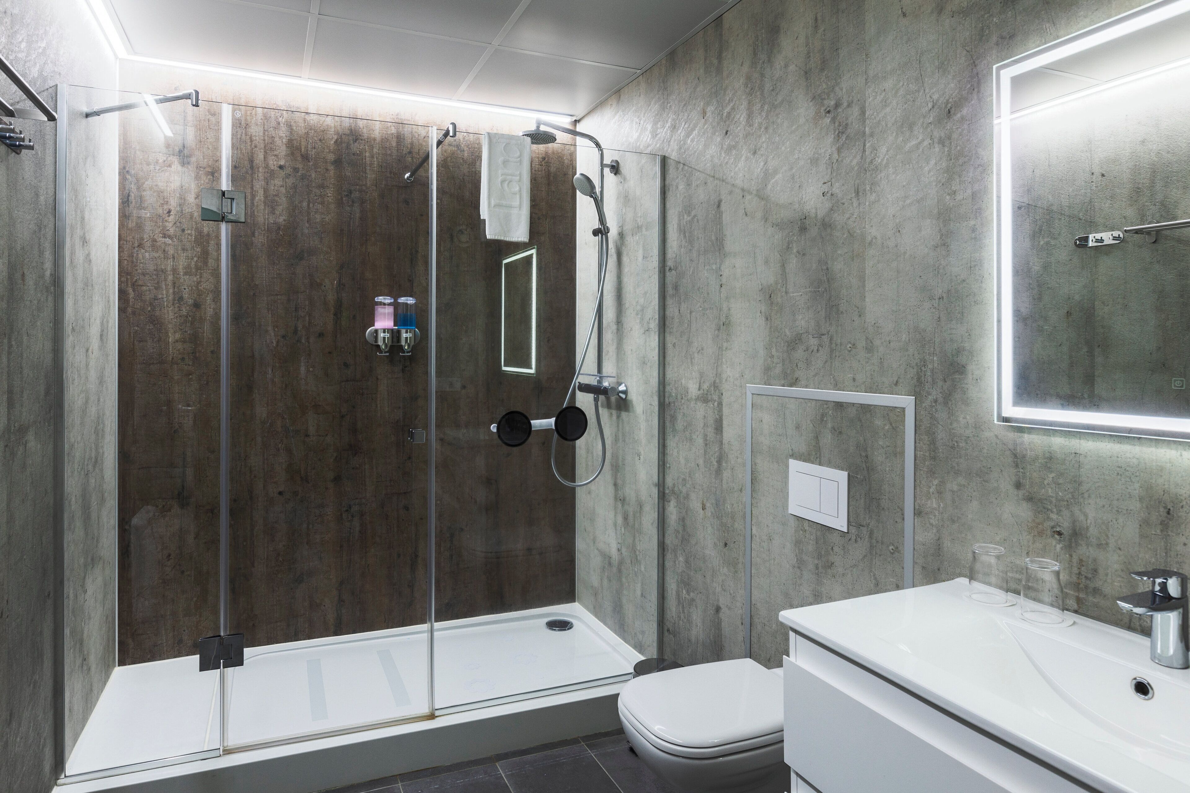Un baño moderno con ducha envuelta en vidrio, inodoro blanco y lavabo con dos vasos en la encimera.