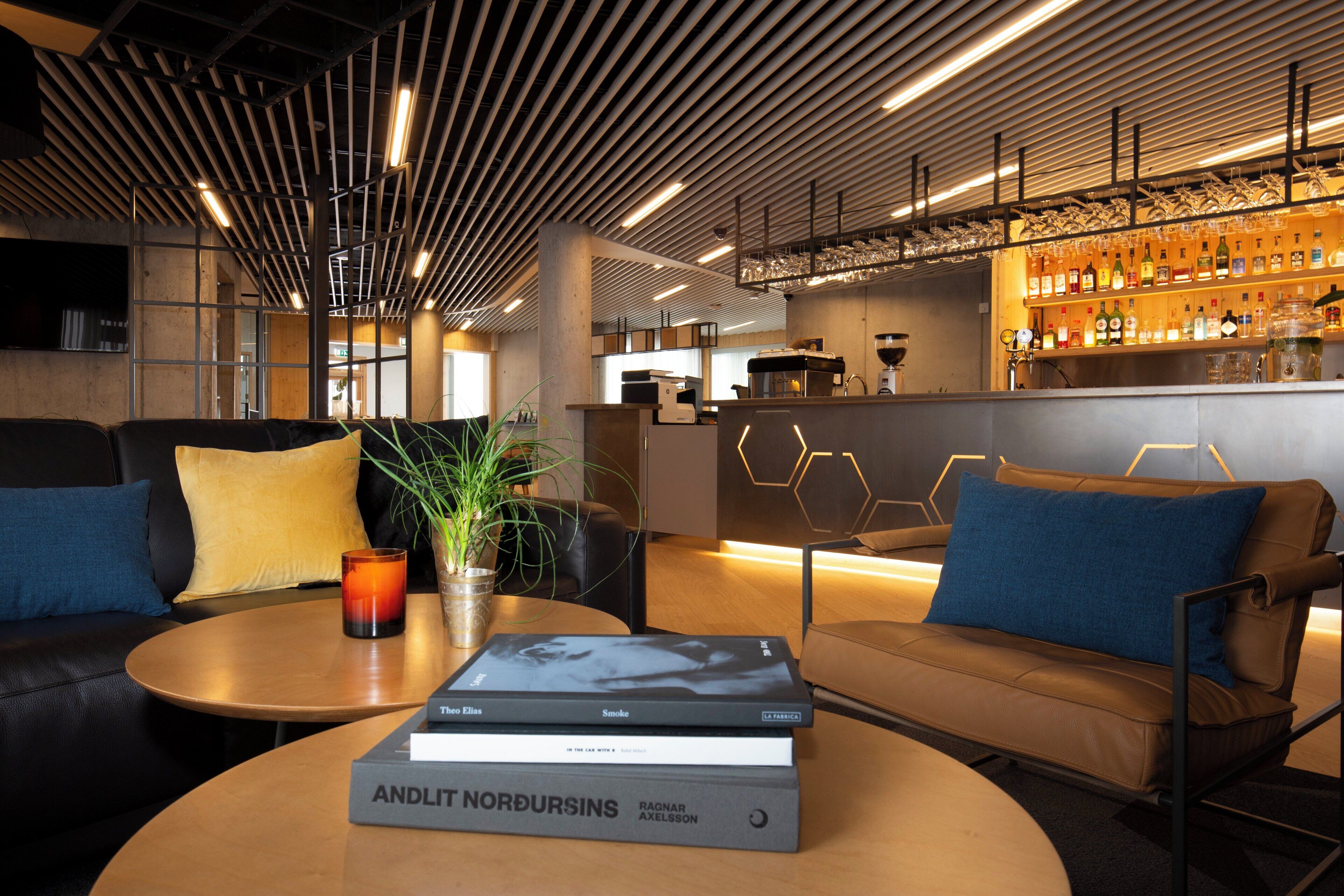A modern bar area with a bar counter, shelves of bottles, and a seating area with leather sofas and a coffee table.