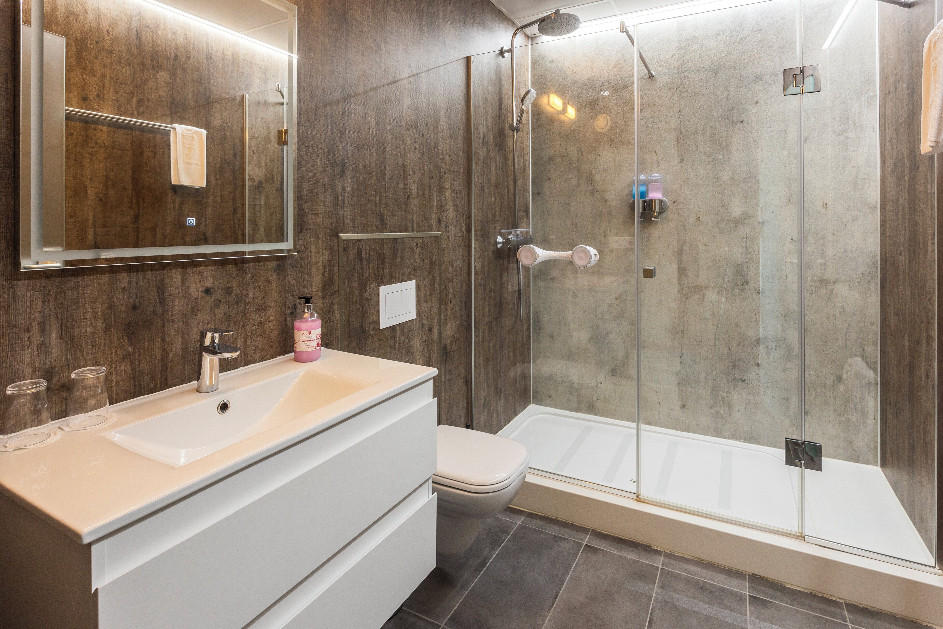 Un baño moderno con ducha de vidrio, un lavabo blanco y un espejo grande.