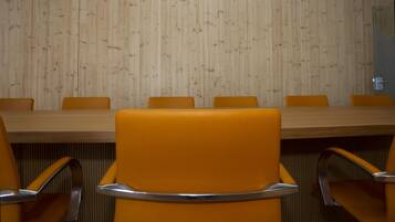 Un salón de conferencias con pared de paneles de madera, una mesa larga y sillas naranja con reposabrazos metálicos.