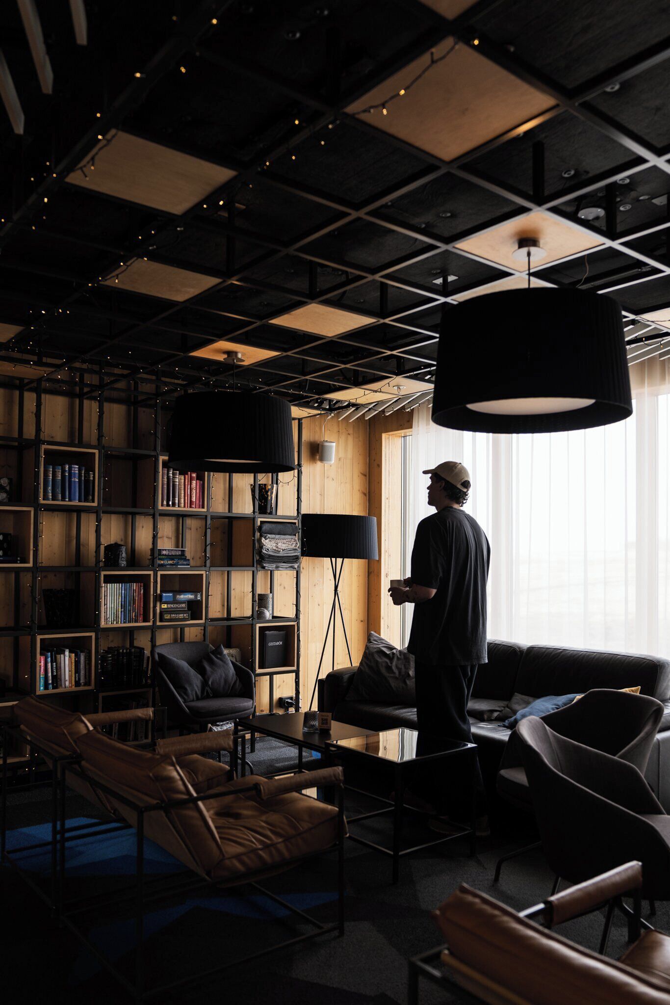 A modern interior with a large bookshelf, leather sofas, and a hanging light fixture.