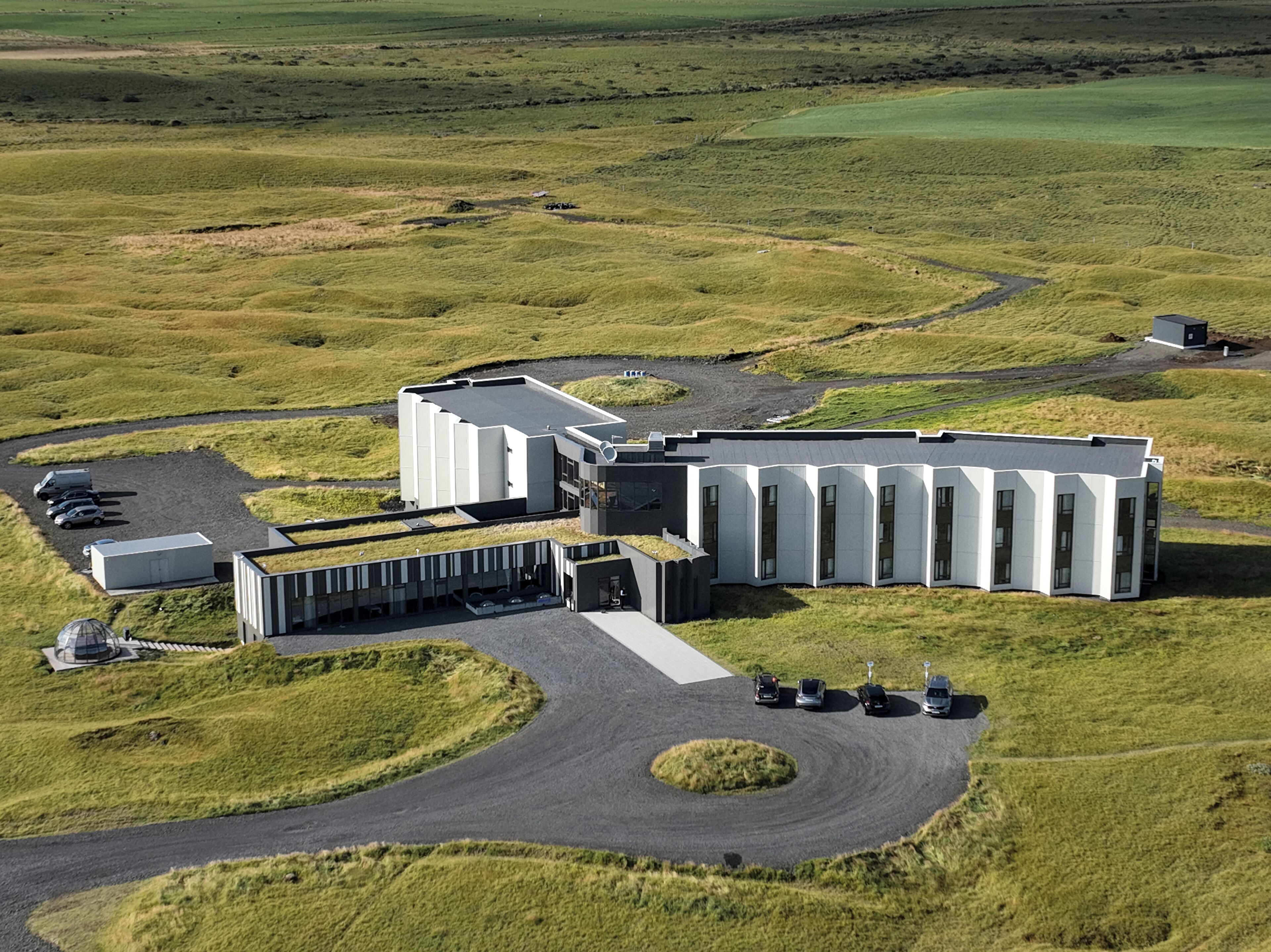 An industrial facility with a modern building, parking area, and a curved road.