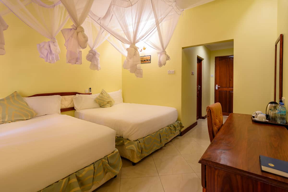 A hotel room with two beds, a wooden desk, and a door leading to another room.