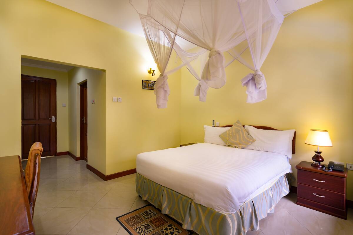 A hotel room with a bed, bedside table, lamp, and a door leading to another room.