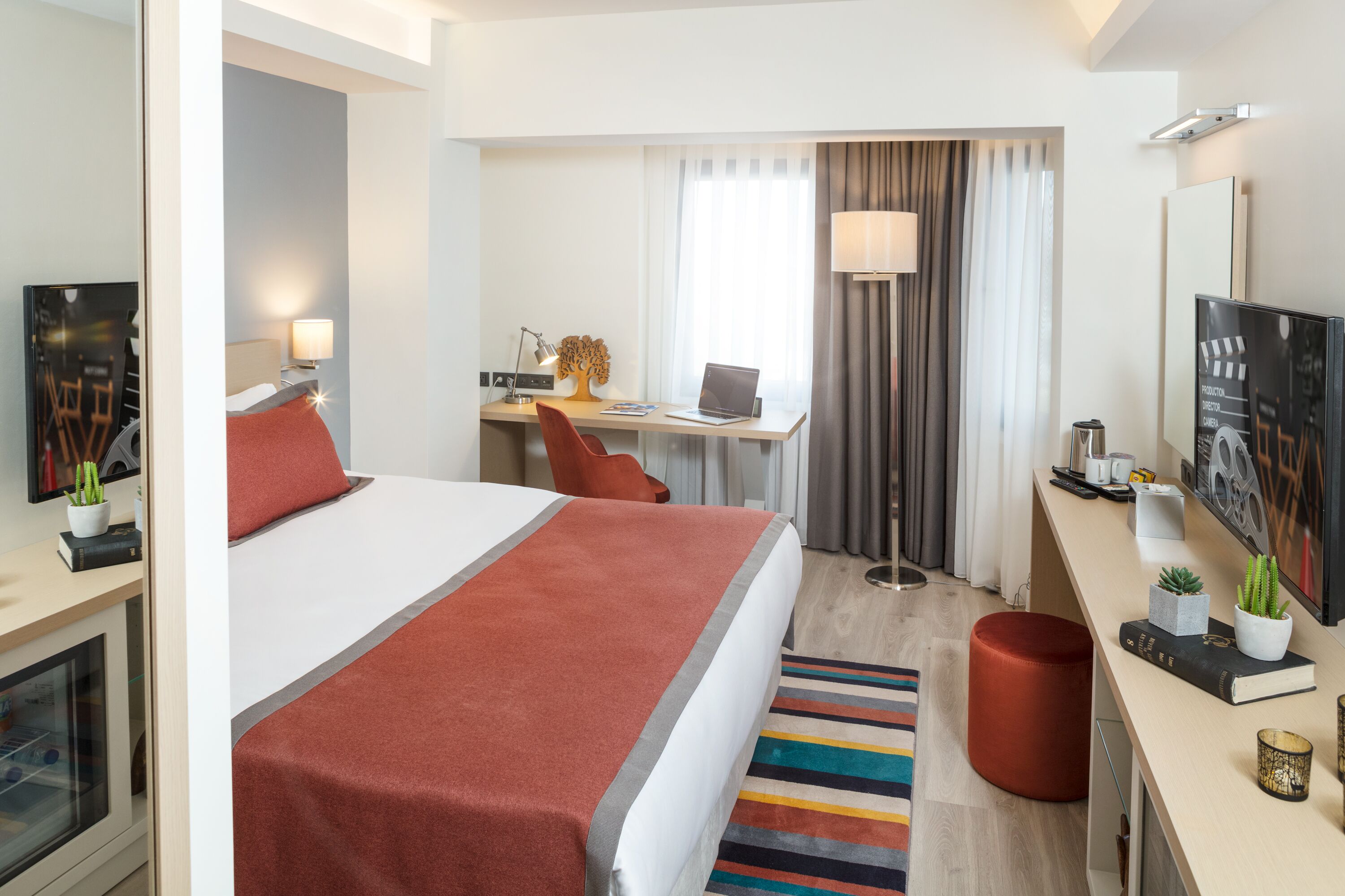 Hotellihuone, jossa on sänky, työpöytä, tuoli, televisio ja pieni kasvi.