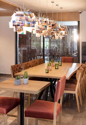 A modern dining area with a long wooden table, cushioned chairs, and a decorative hanging light fixture. - TRYP by Wyndham Ankara Oran (Ankara)