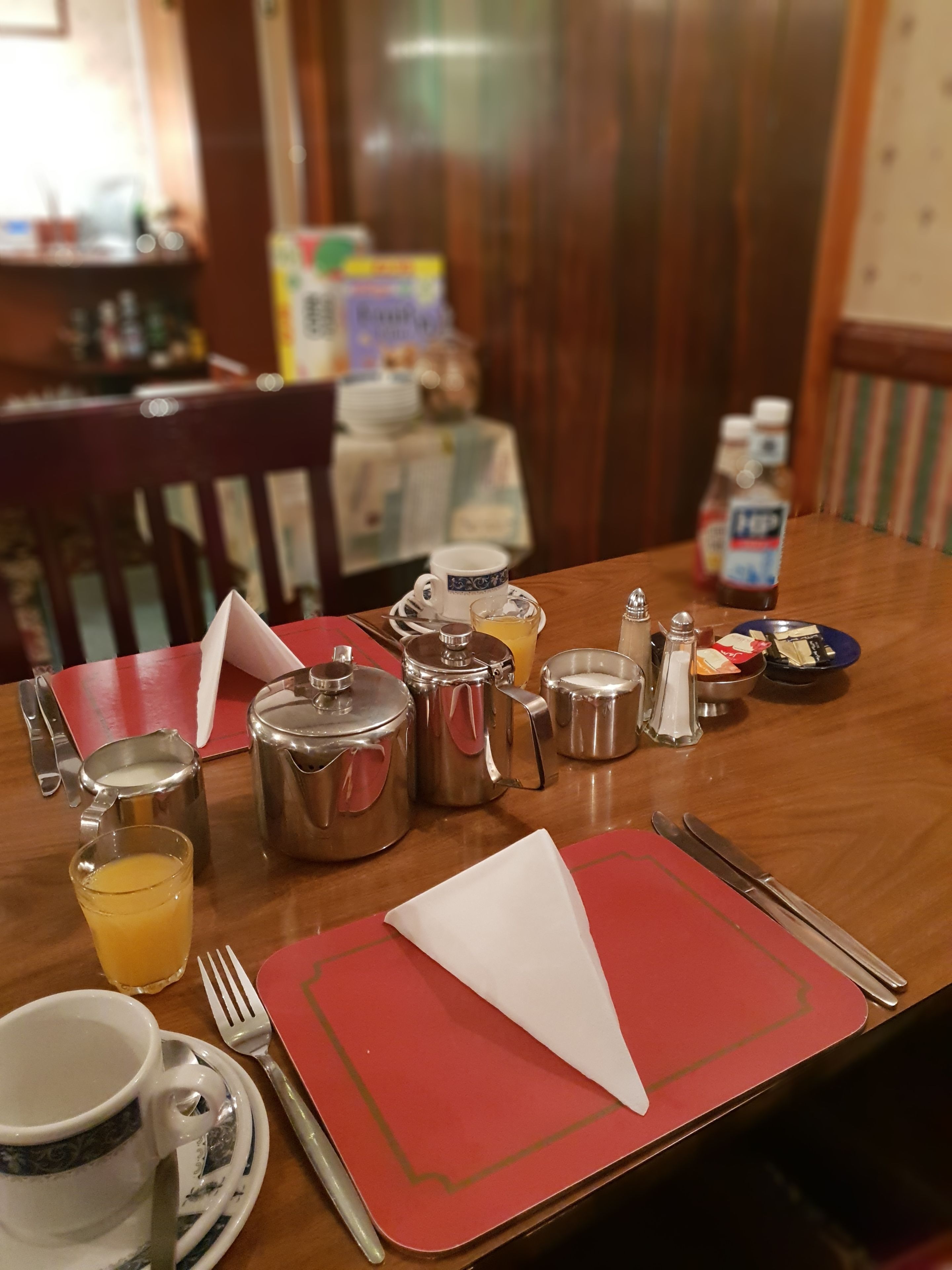 A dining table set with various breakfast items including a jug of orange juice, a teapot, a sugar bowl, and a plate of food.