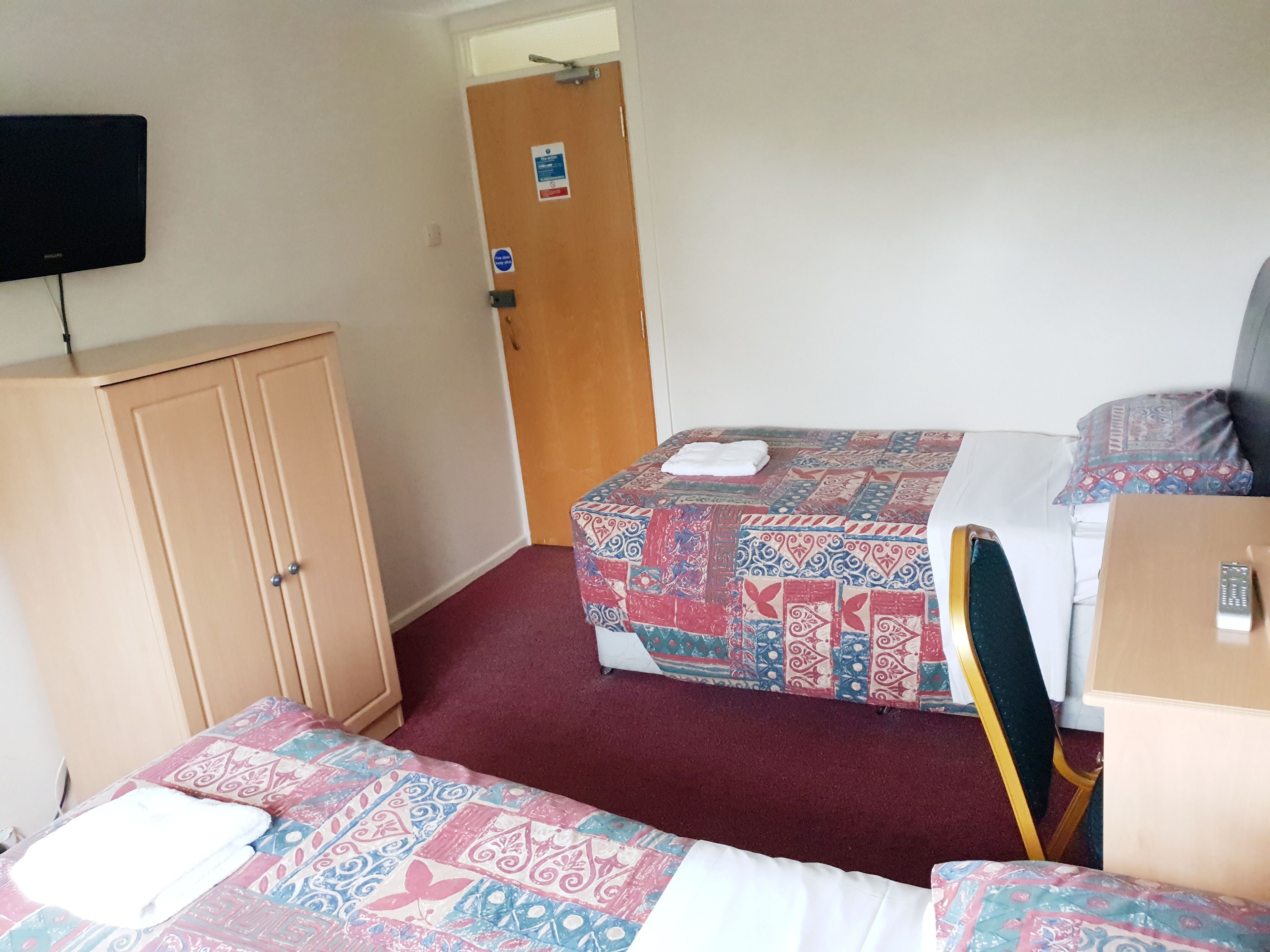 A room with two beds, a wardrobe, a television, and a door with a sign.