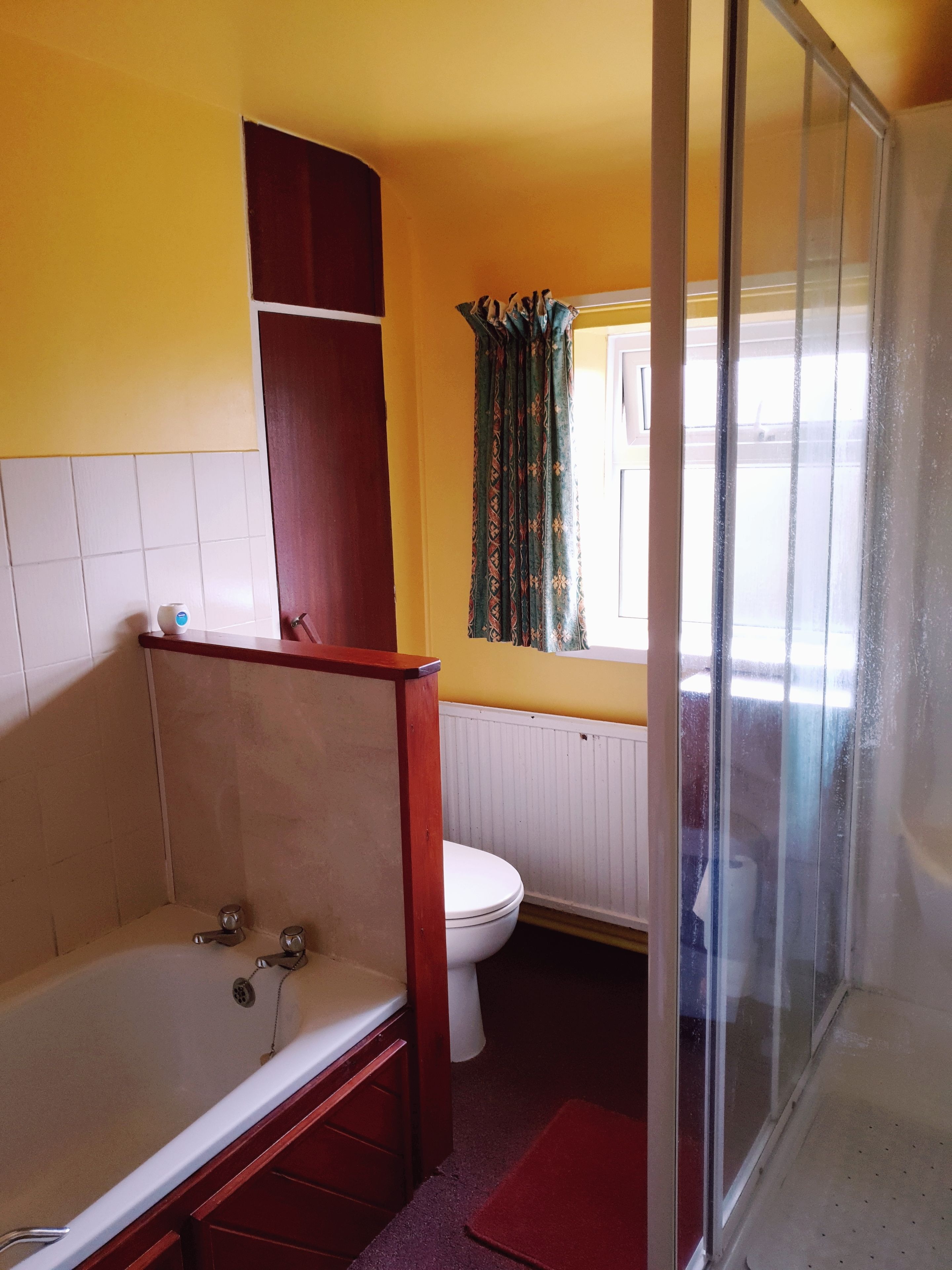 A bathroom with a bathtub, toilet, and a window with curtains.