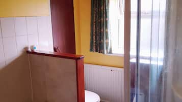 A bathroom with a bathtub, toilet, and a window with curtains.