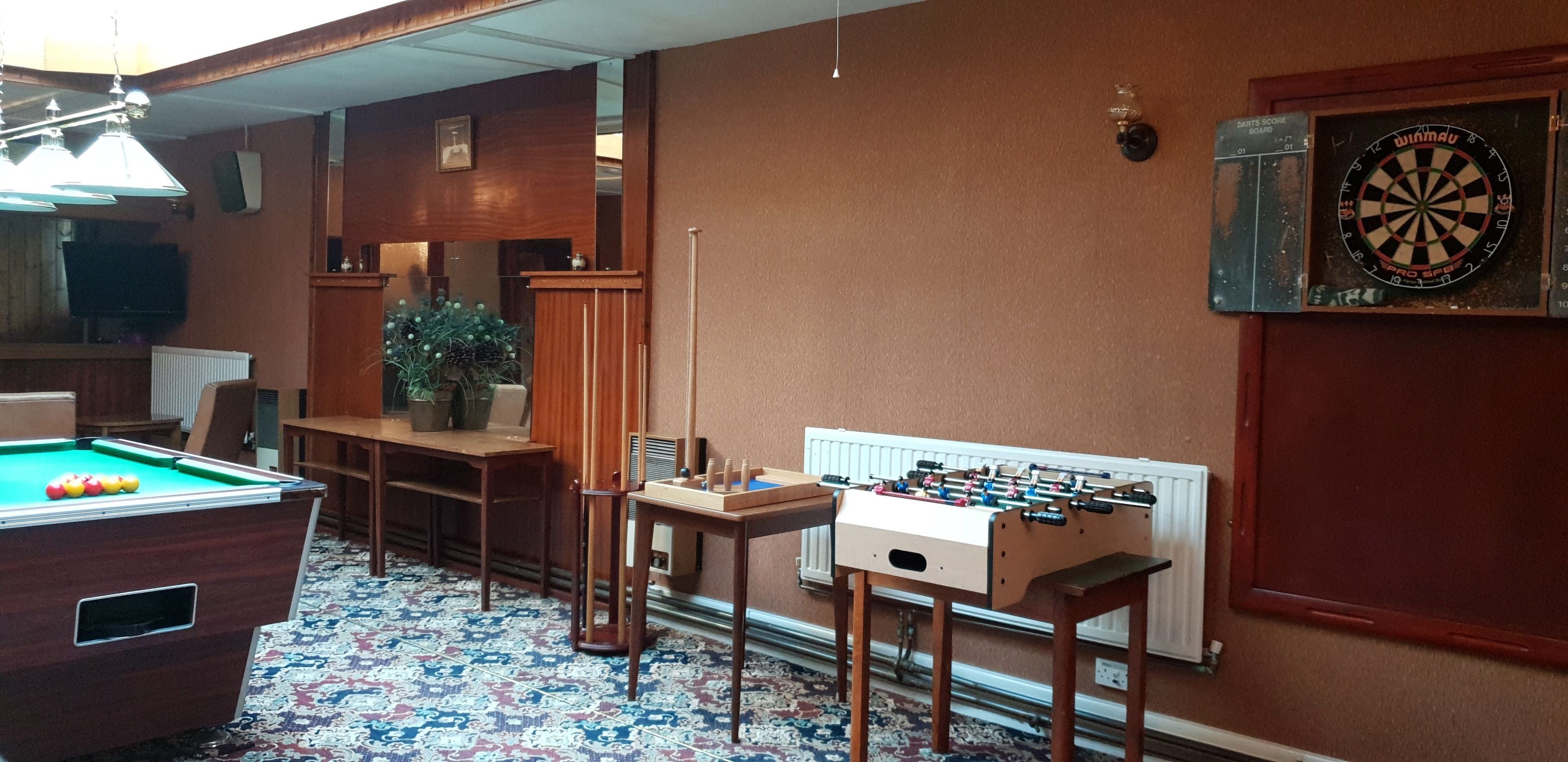A room with a pool table, foosball table, dartboard, and a television.