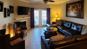 A living room with a black leather sofa, a coffee table, a TV, and a fireplace.